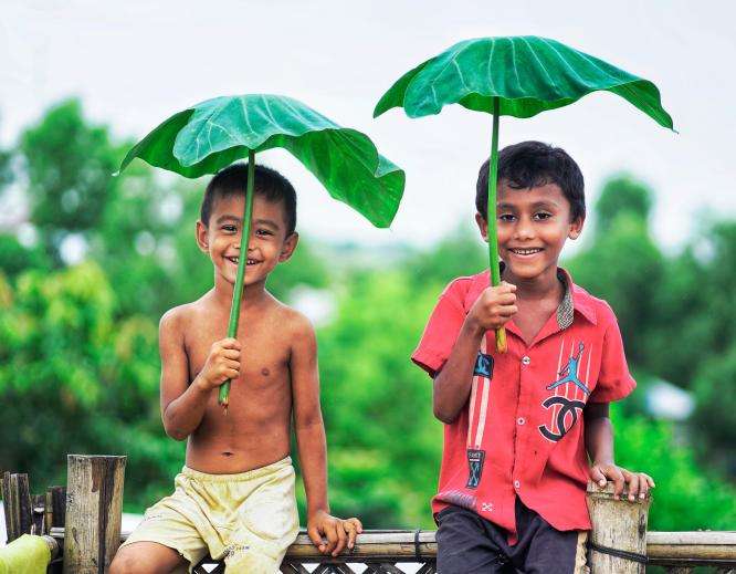 Two boys hold taro leaves above their heads in Bangladesh.
